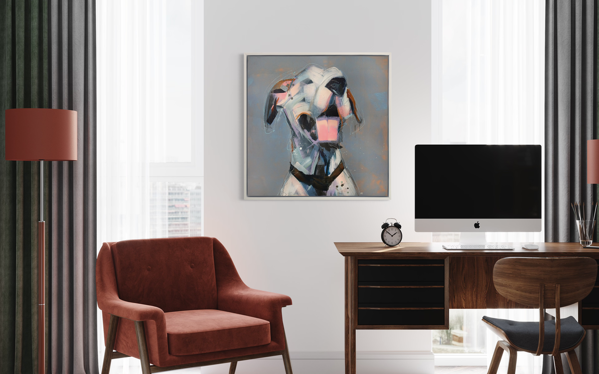 A white, light pink, grey and brown abstract dog print in a white floater frame hangs on a white wall above a wood desk with a large computer monitor, an alarm clock, a wood desk chair and rust colored armchair to the side.