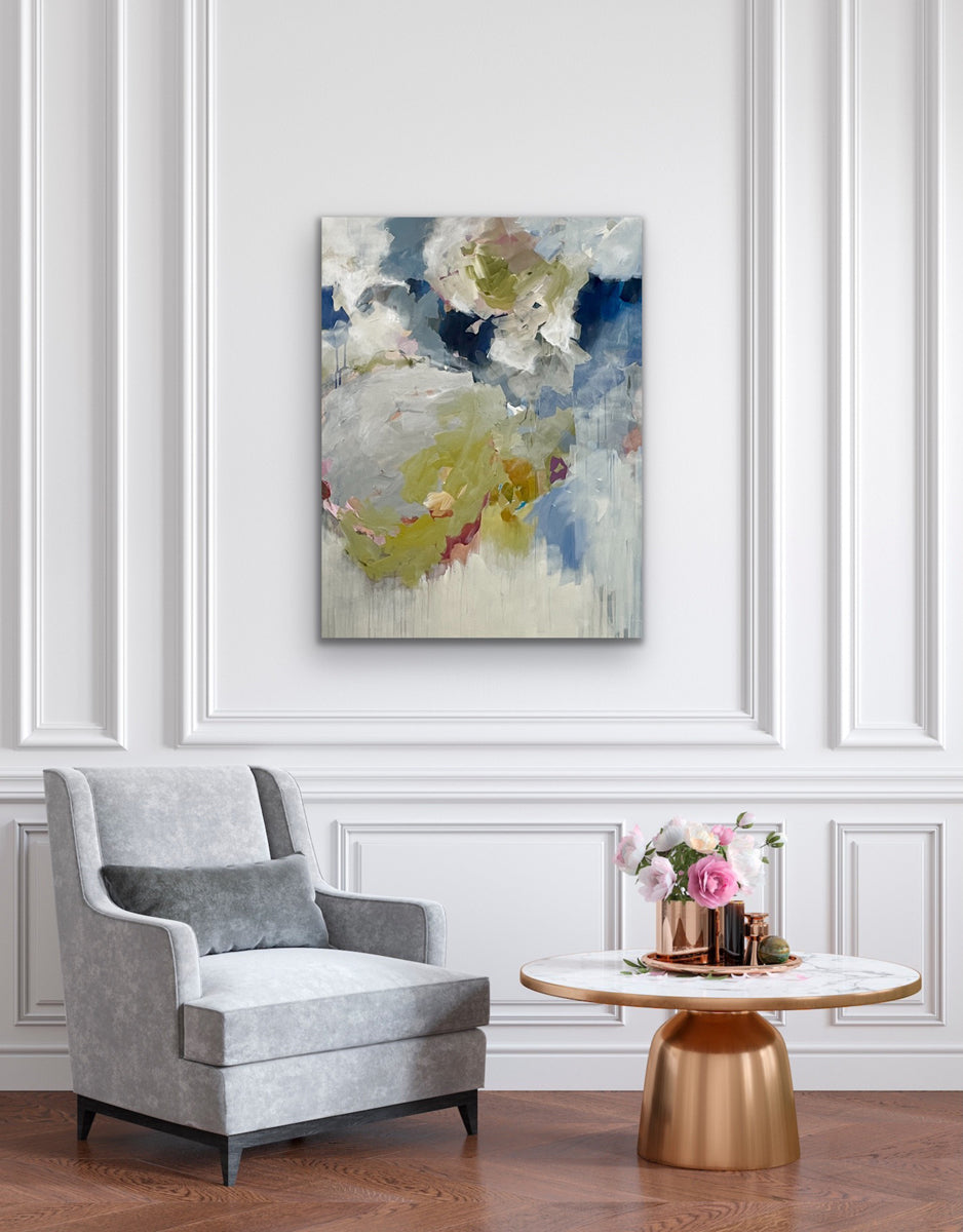 Gray armchair in a room with a abstract painting on the wall and a small table with decor items.
