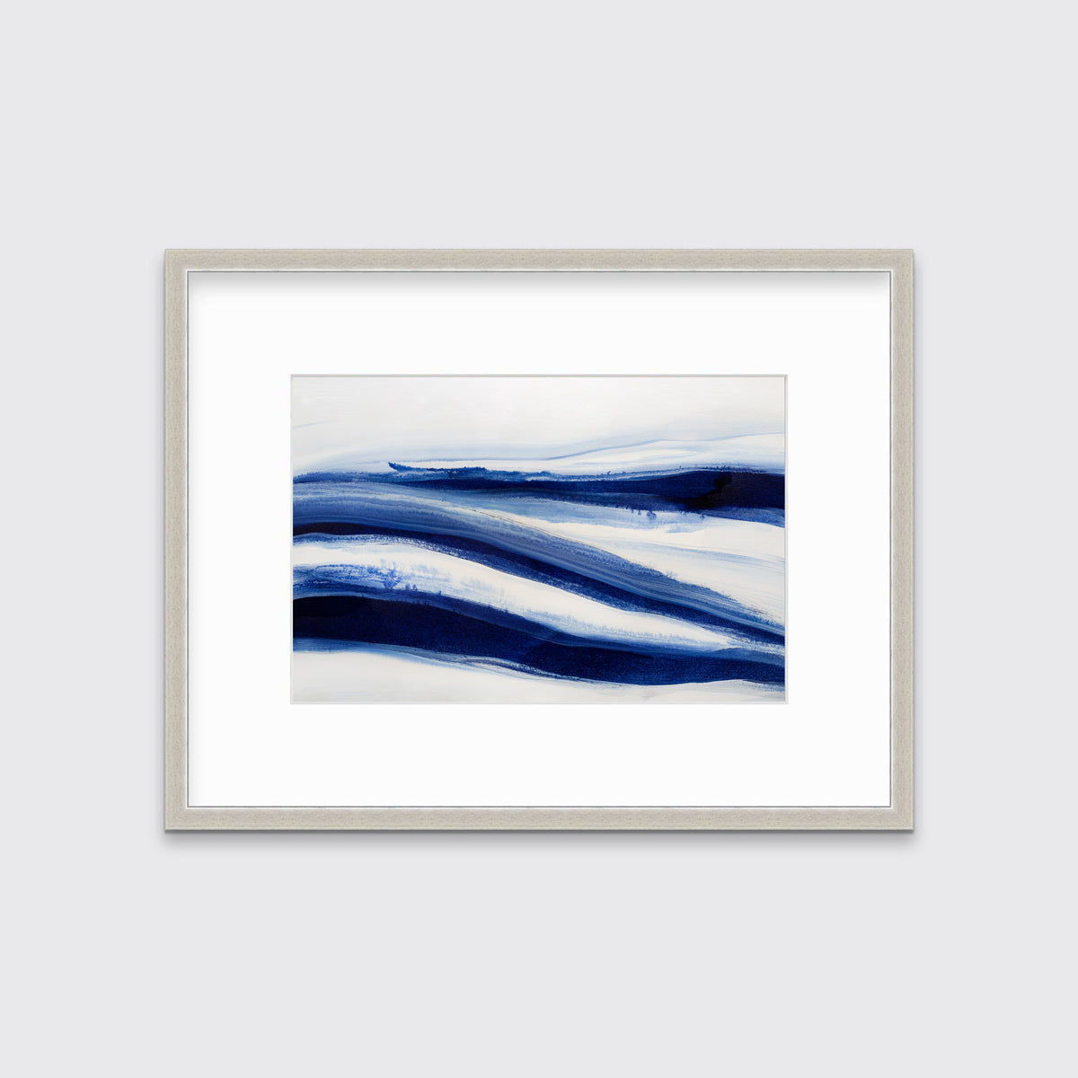 A dark blue and white abstract print in a silver frame with a mat hangs on a white wall.