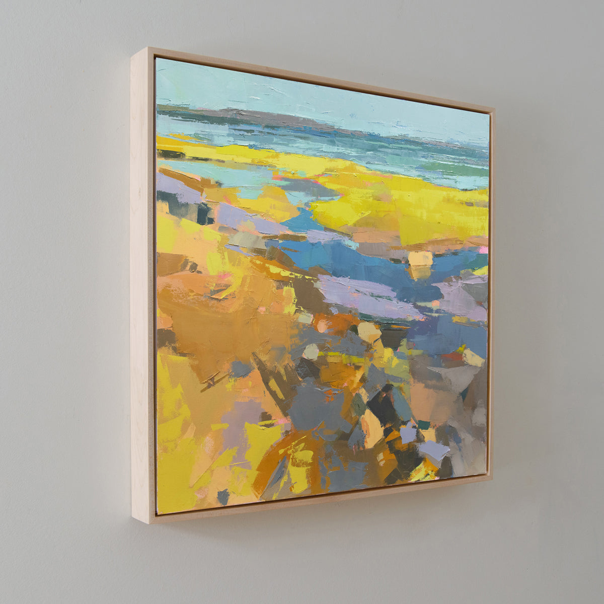 A blue and yellow abstract landscape painting hangs on a white wall at an angle. 