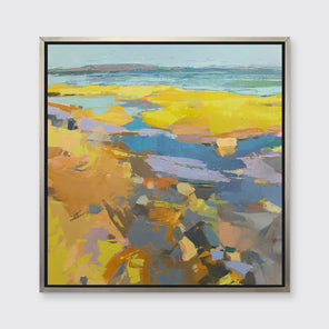 A yellow abstracted landscape print framed in a silver frame hangs on a white wall. 