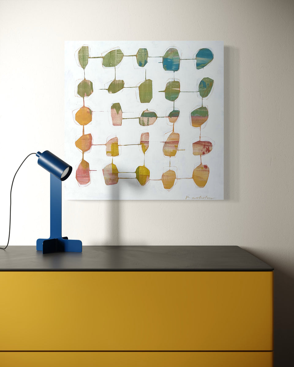 An abstract painting hangs on a light wall above a mustard yellow table with a blue modern table lamp. 
