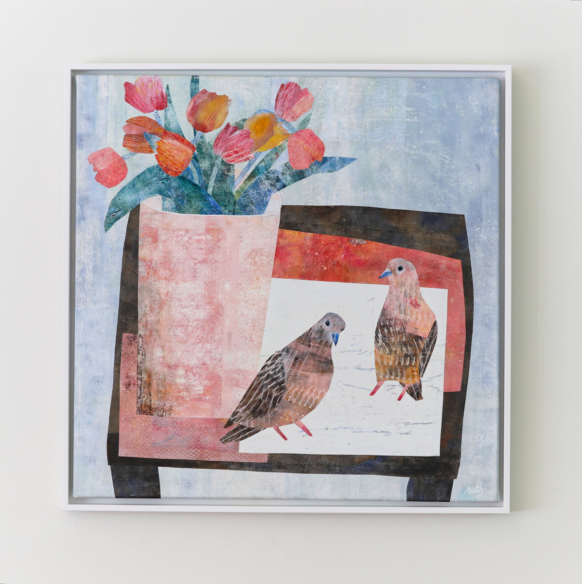 A framed collage featuring two birds and a vase of tulips, displayed on a light beige wall.