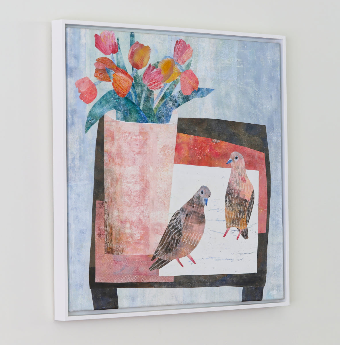 A framed collage featuring two birds and a vase of tulips, displayed on a light gray wall.