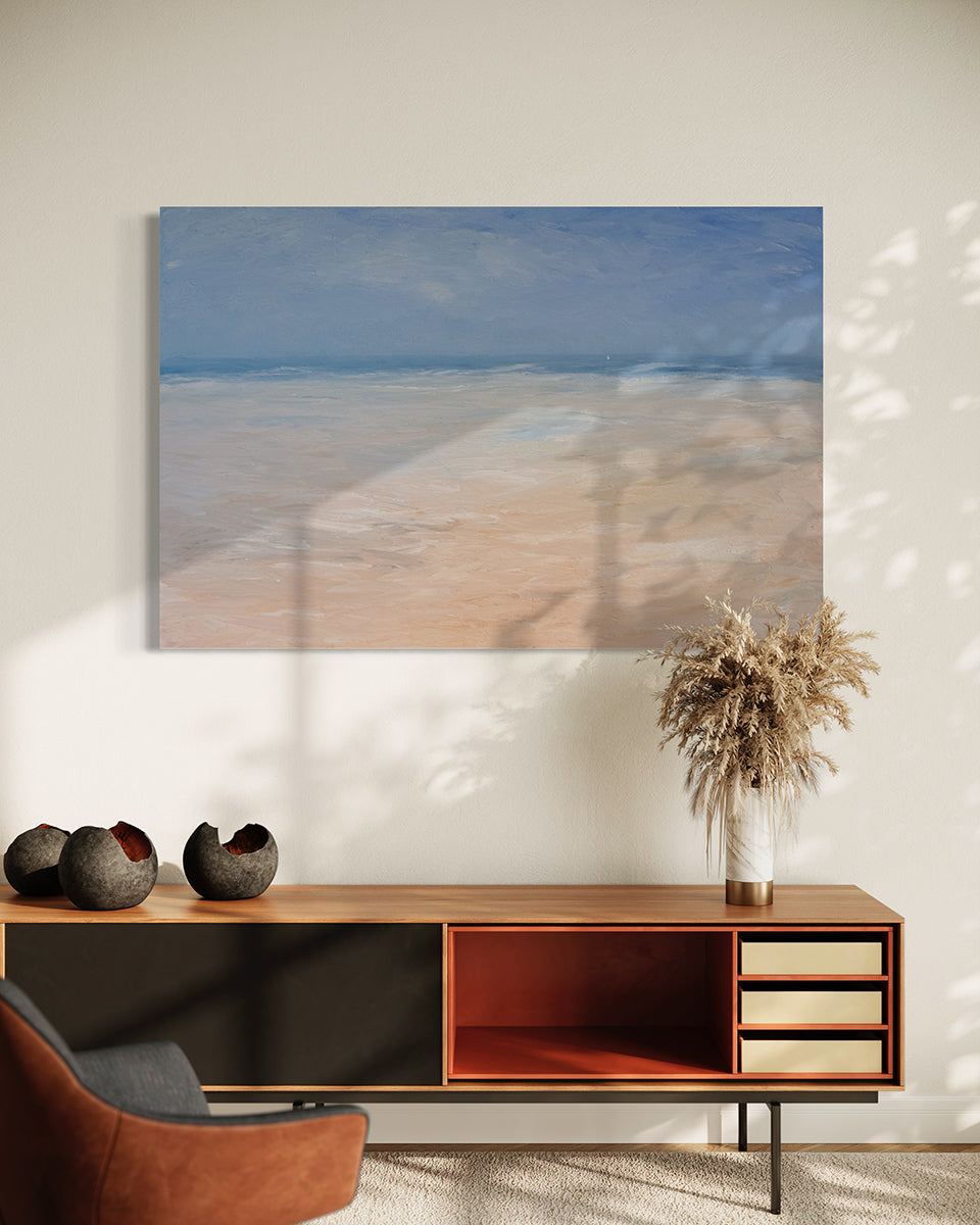 An abstracted coastal seascape painting hangs on white wall above a mid-century modern low credenza. A white vase with dried branches sits to the right and 3 circular ceramic grey sculptures are to the left. 