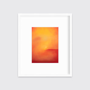 An orange and red abstract print in a white frame with a mat hangs on a white wall.