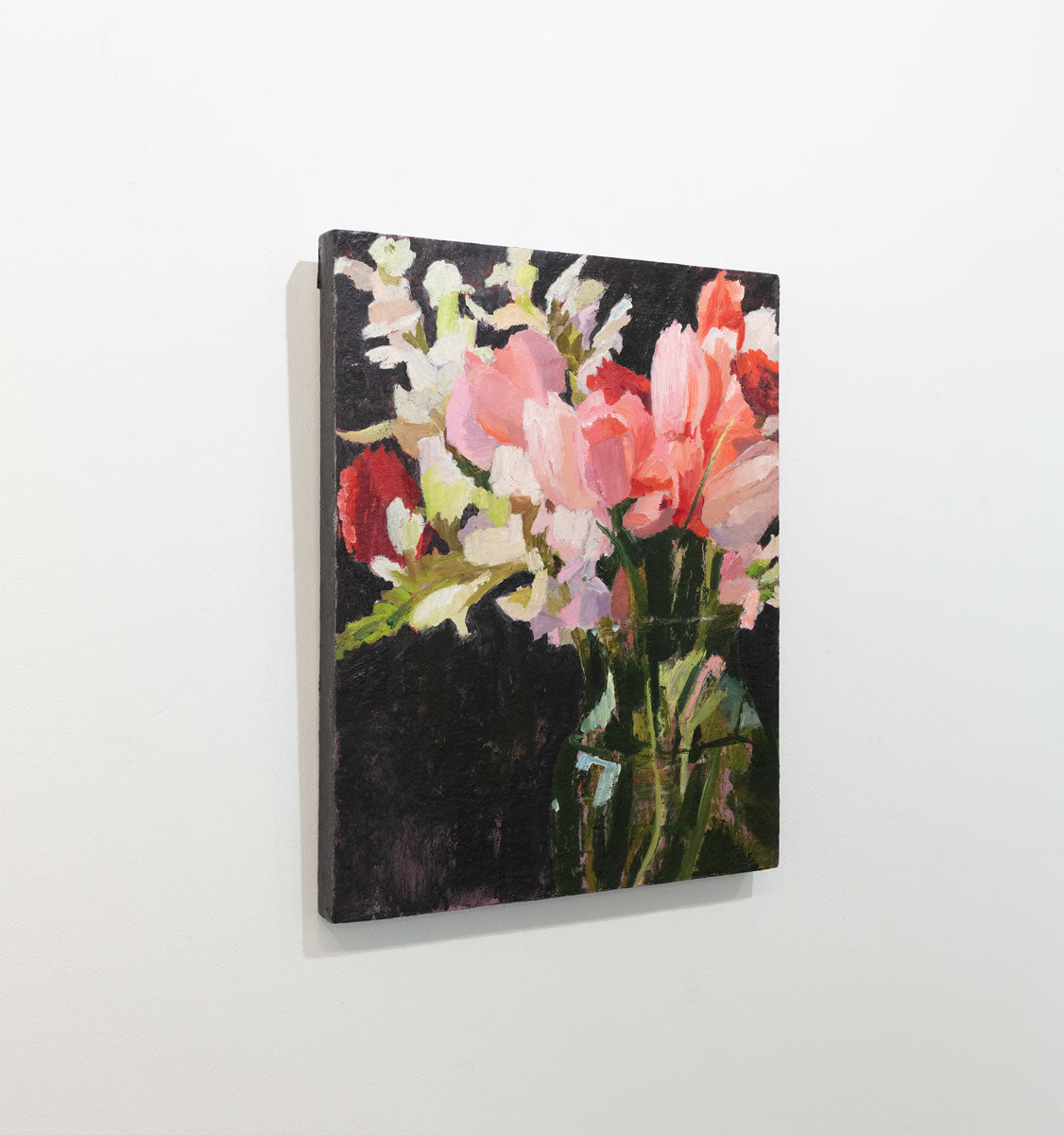 An oil painting of an abstract pink, red and white floral bouquet hangs on a angle on a white wall.