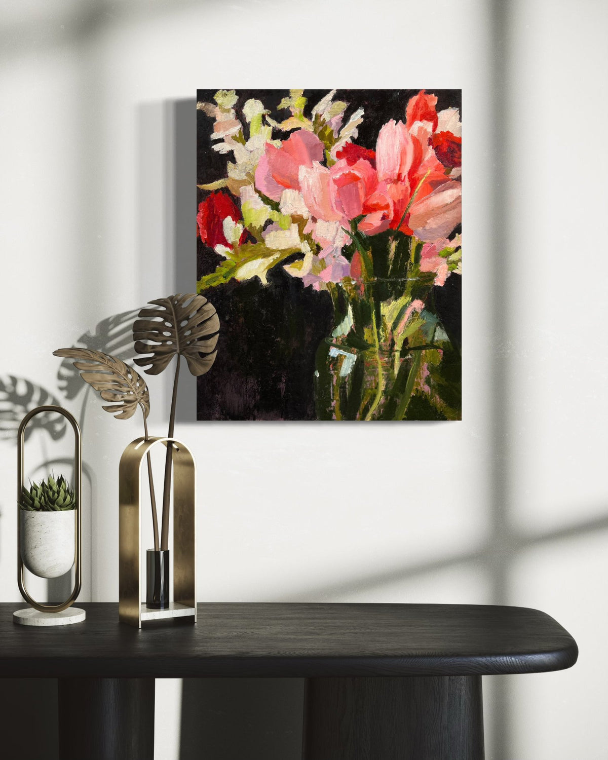 An oil painting of an abstract pink, red and white floral bouquet hanging on a wall over a black credenza with metal floral decorative objects.