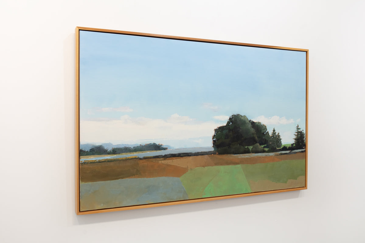 A blue, green, and sienna-toned landscape painting in a light wood frame hangs on a white wall.