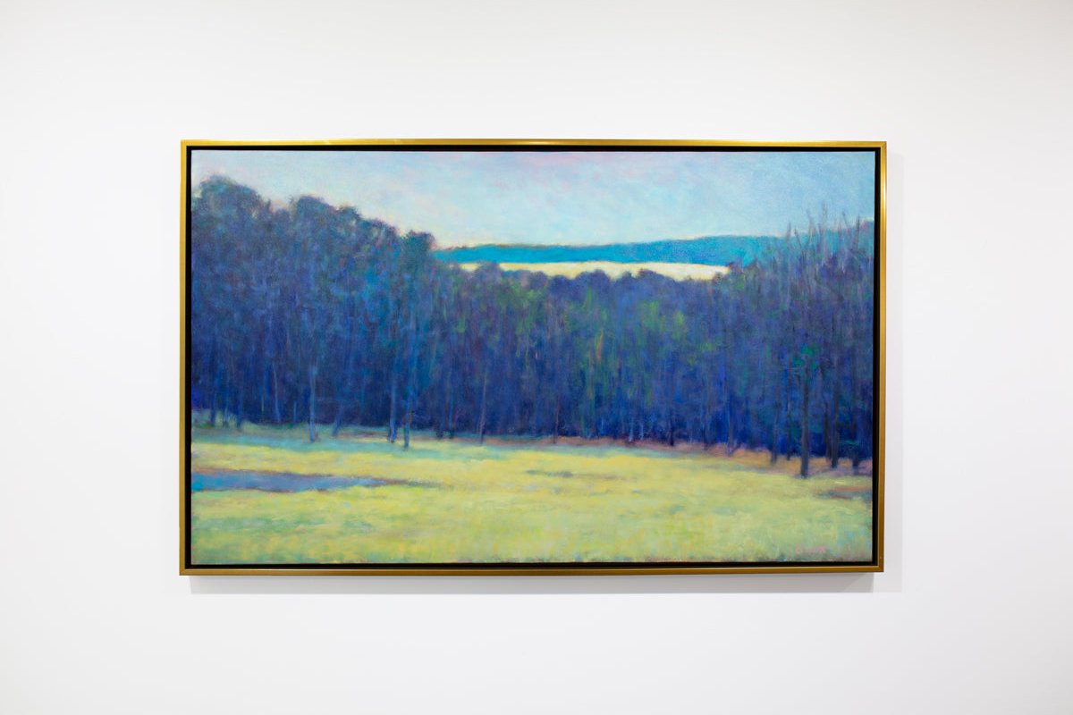 A blue, teal and chartreuse abstract landscape painting by Ken Elliott hangs in a gold faced frame on a white wall.