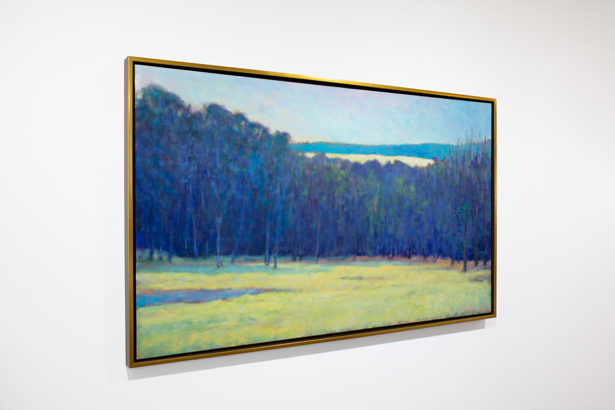 A side view of a blue, teal and chartreuse abstract landscape painting by Ken Elliott hangs in a gold faced frame on a white wall.