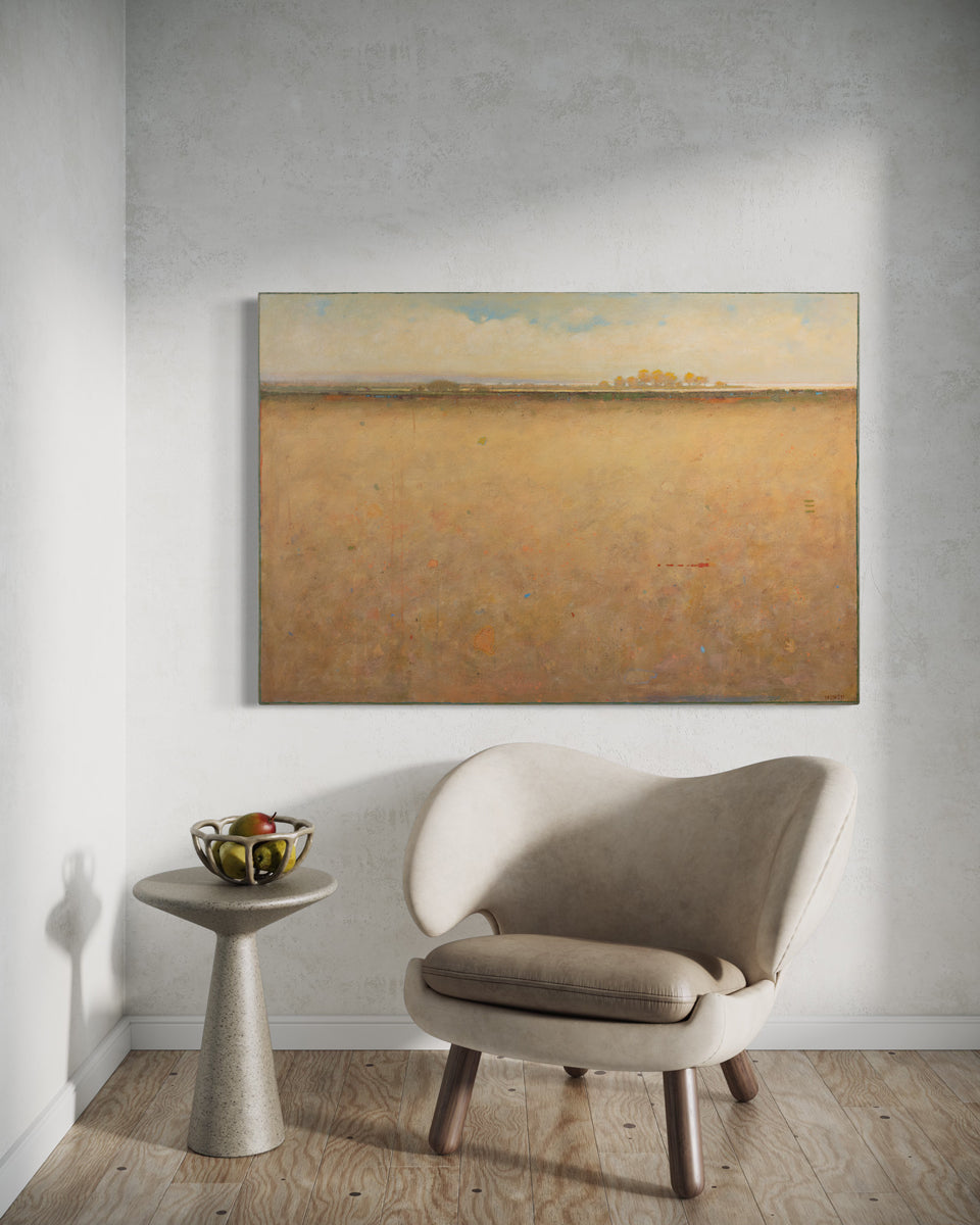 A beige and blue abstract landscape painting hangs on a white wall above a grey modern armchair and a marble pedestal table with a basket of fruit.