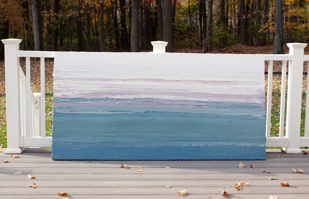 A white, lavender, teal and blue abstract heavily textured painting like sculpture by Teodora Guererra leaning outside in natural light on a deck.