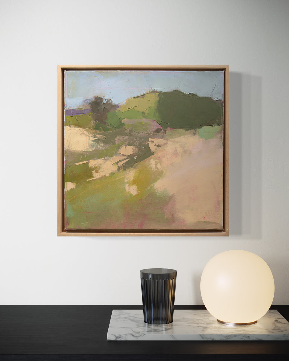 A framed green and warm beige abstracted landscape painting hangs on a white wall above a black wood table surface with a marble tray, orb light, and black glass. 