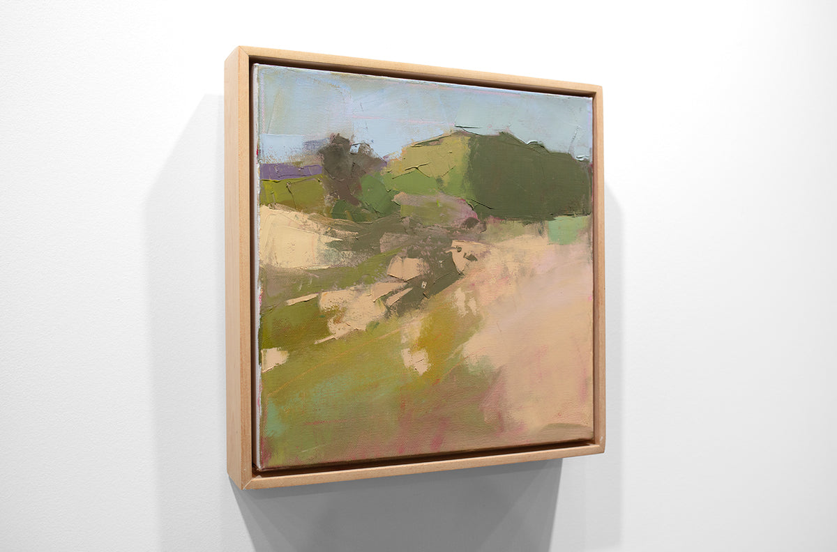 A framed green and warm beige abstracted landscape painting hangs on a white wall.
