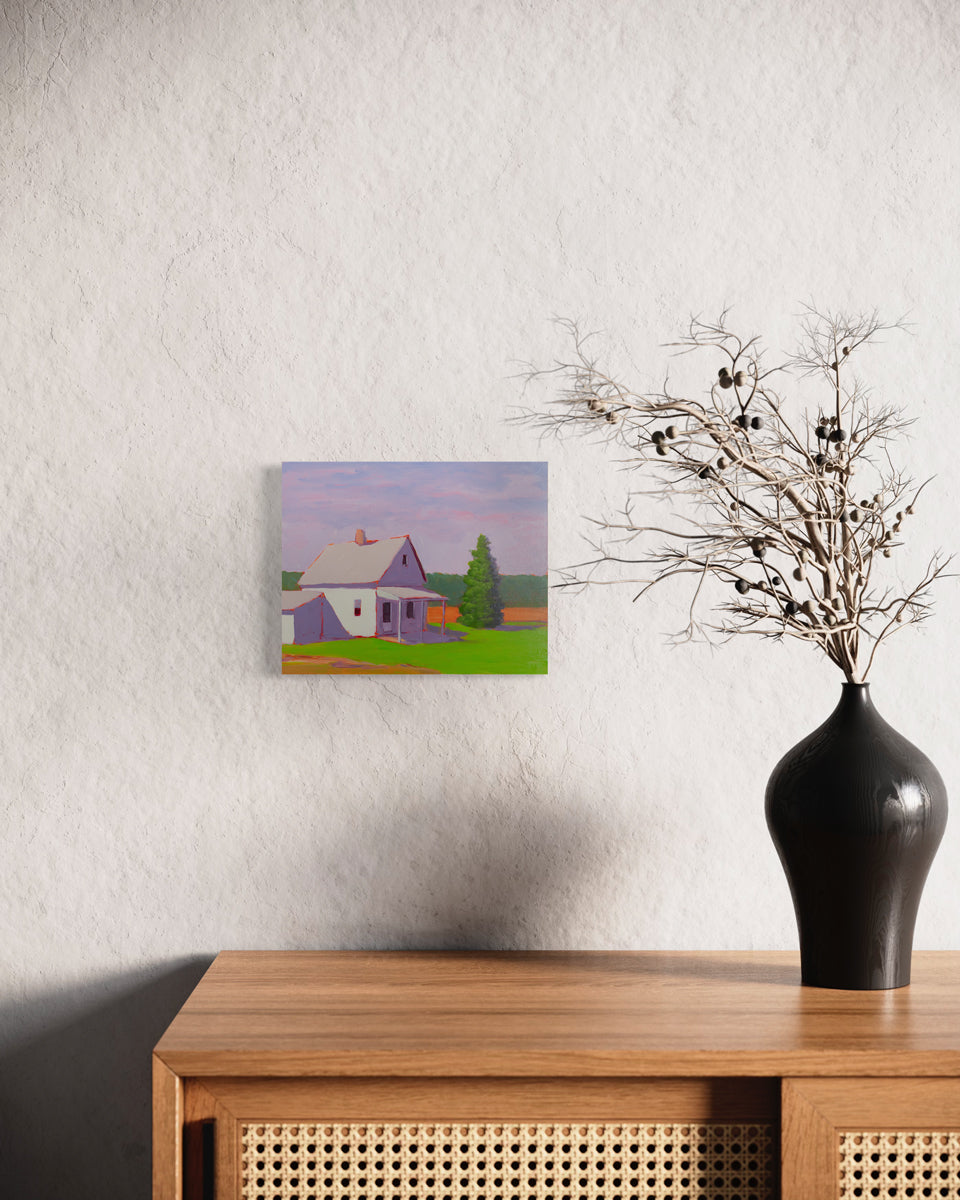 A small purple, green, and orange landscape painting hangs on a textured white wall above a wooden console table with a black modern vase with tried plants.