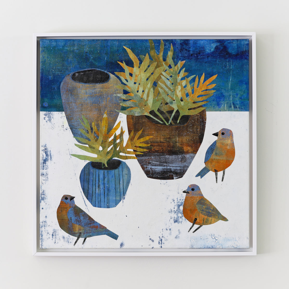 A framed square collage featuring a still life of blue and brown vases with green-yellow ferns and three small birds in shades of blue, orange, and gray, displayed on a light wall.