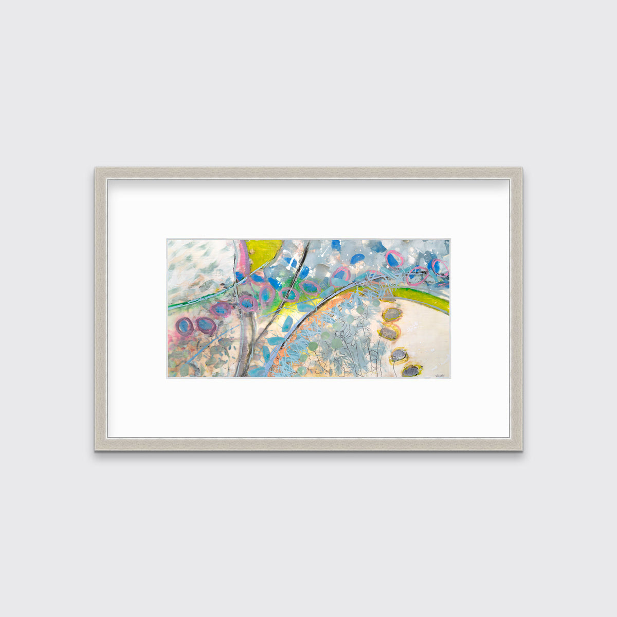 A multicolored abstract print in a silver frame with a mat hangs on a white wall.
