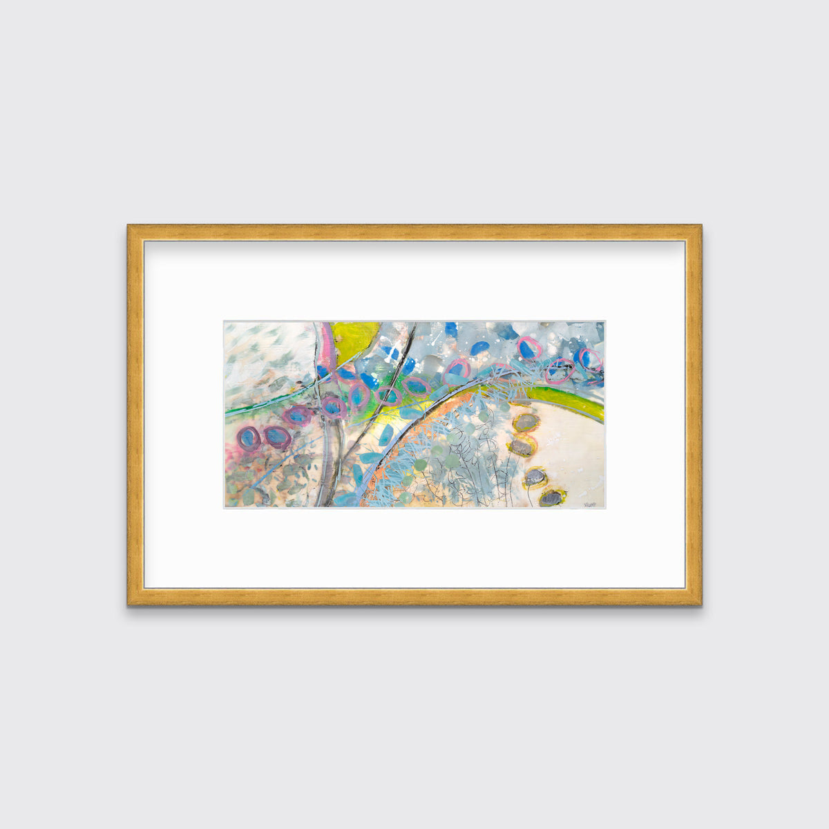 A multicolored abstract print in a gold frame with a mat hangs on a white wall.