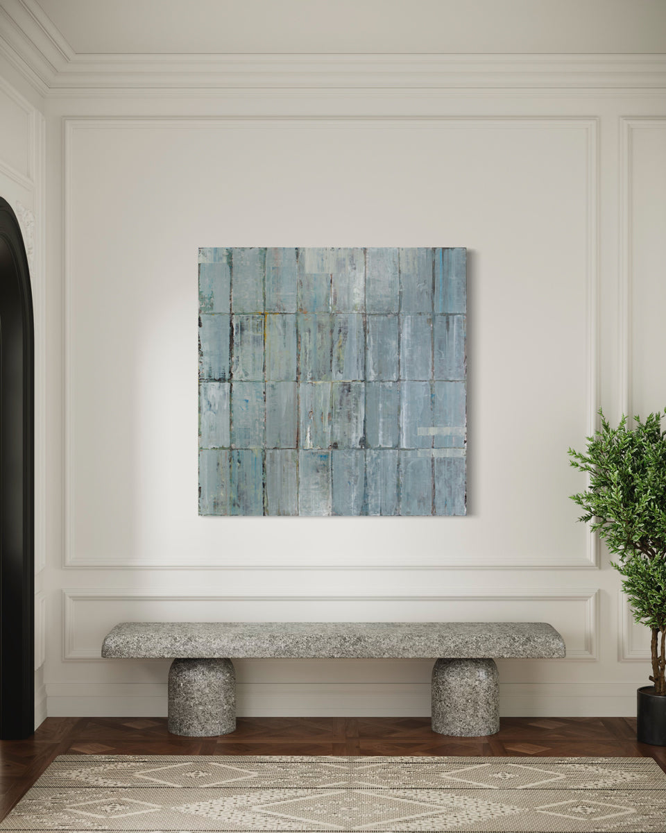 A blue and grey abstract geometric painting hangs on a white wall above an interior stone bench and floor plant. 