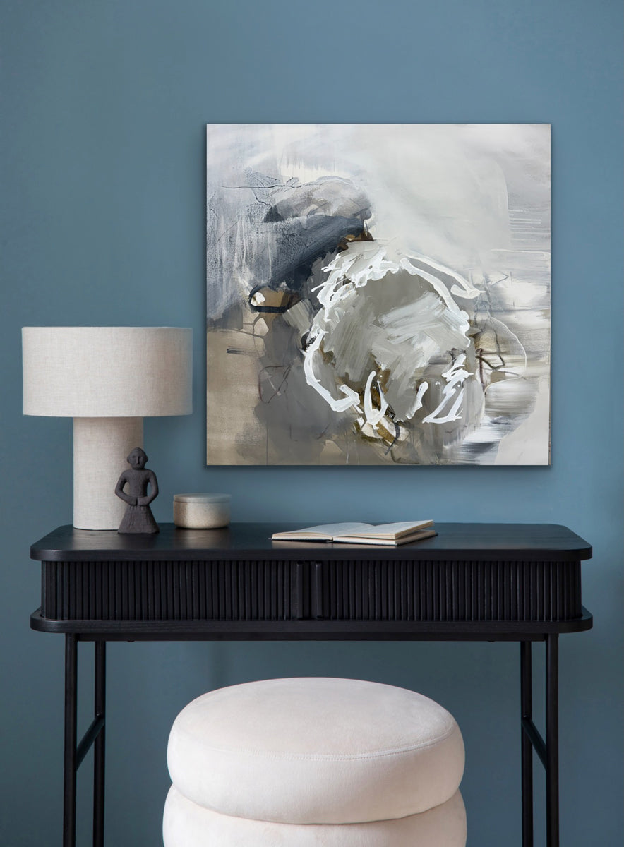 Abstract painting on a blue wall above a black console table with decor items.