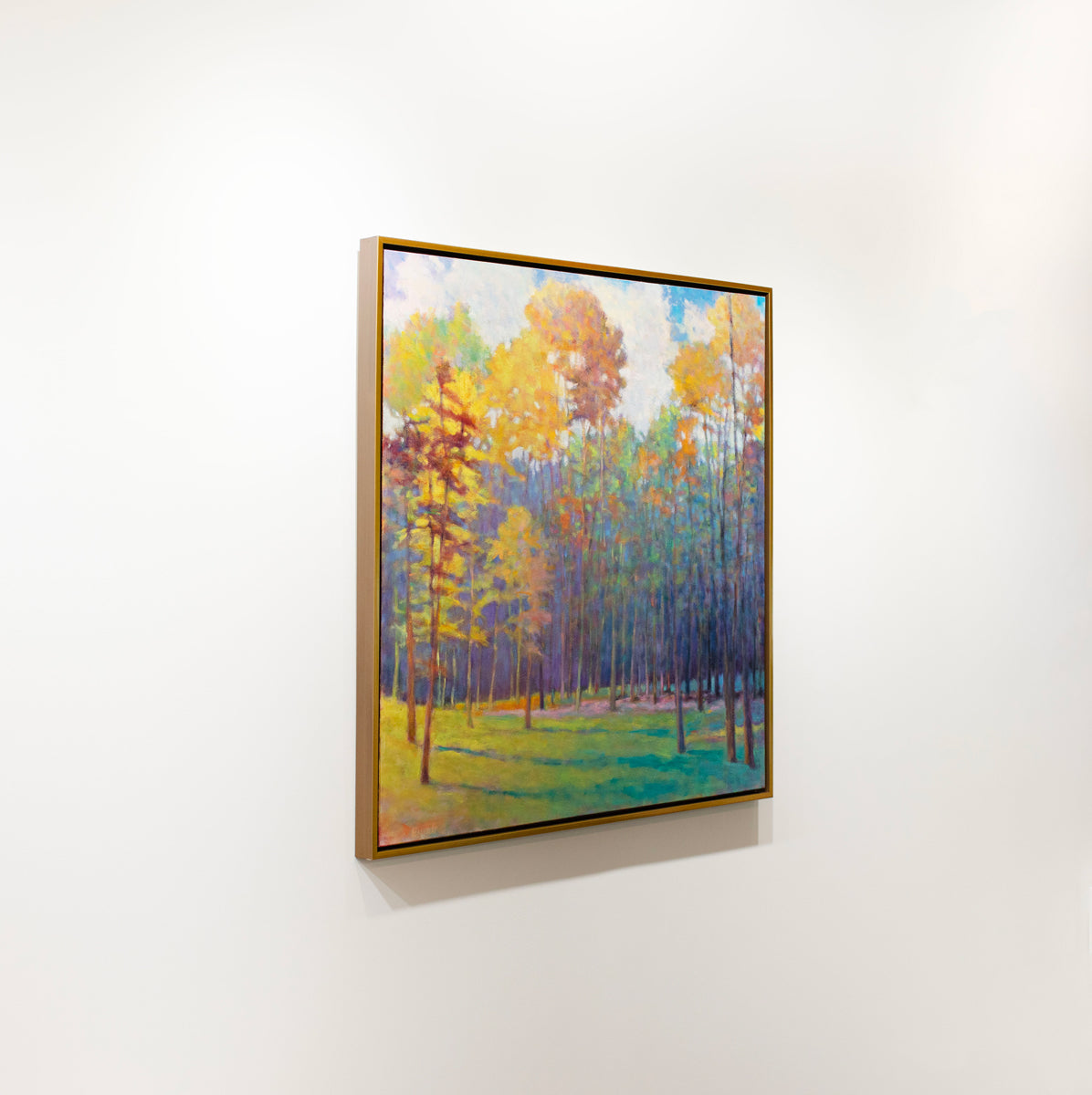 A colorful abstracted landscape painting framed in a thin gold floater frame hangs on a white wall.