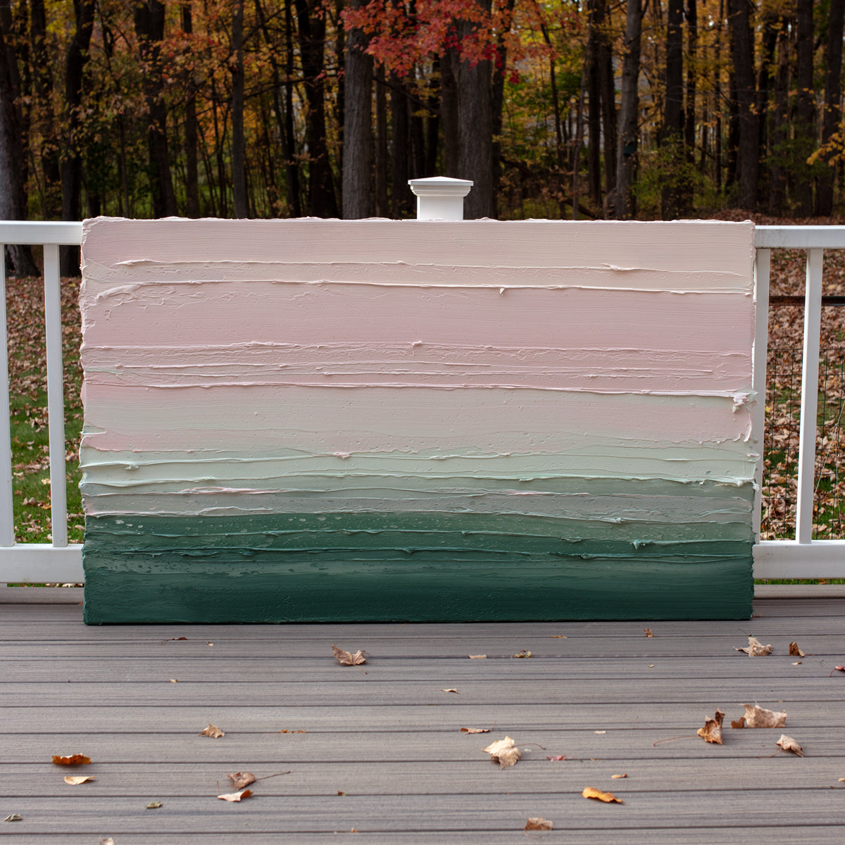A light Coral, light pink, celadon and hunter green thickly textured abstract painting by Teodora Guererra leaning outside on a deck.