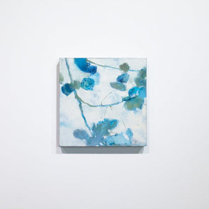 A white and blue abstract floral painting hangs on a white wall. 