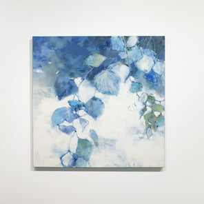 A blue and white abstract floral painting hangs on a white wall. 