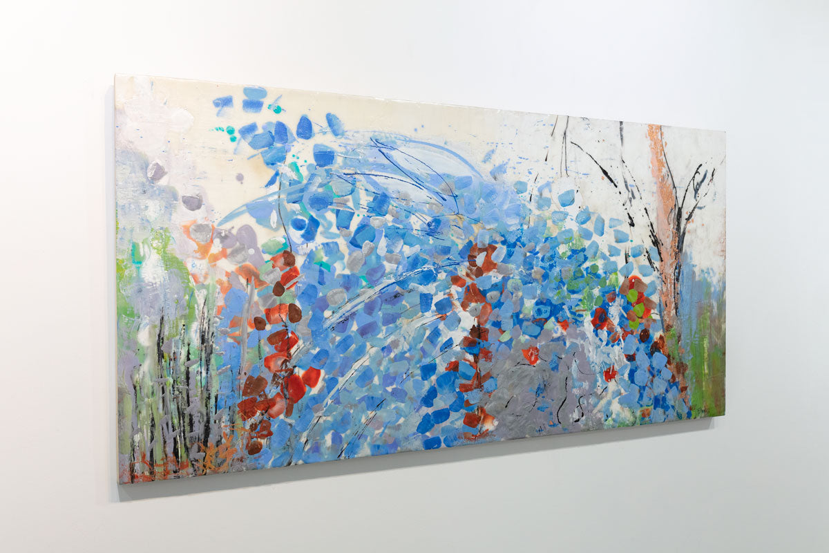 An encaustic painting with expressionistic floral motifs in red and blue is seen at an angle on a gallery wall. Wired and ready to hang.