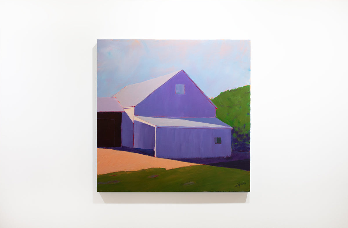 A landscape painting of a barn in lavender shadow, blue sky and green hedges by Carol Young hangs on a white wall.