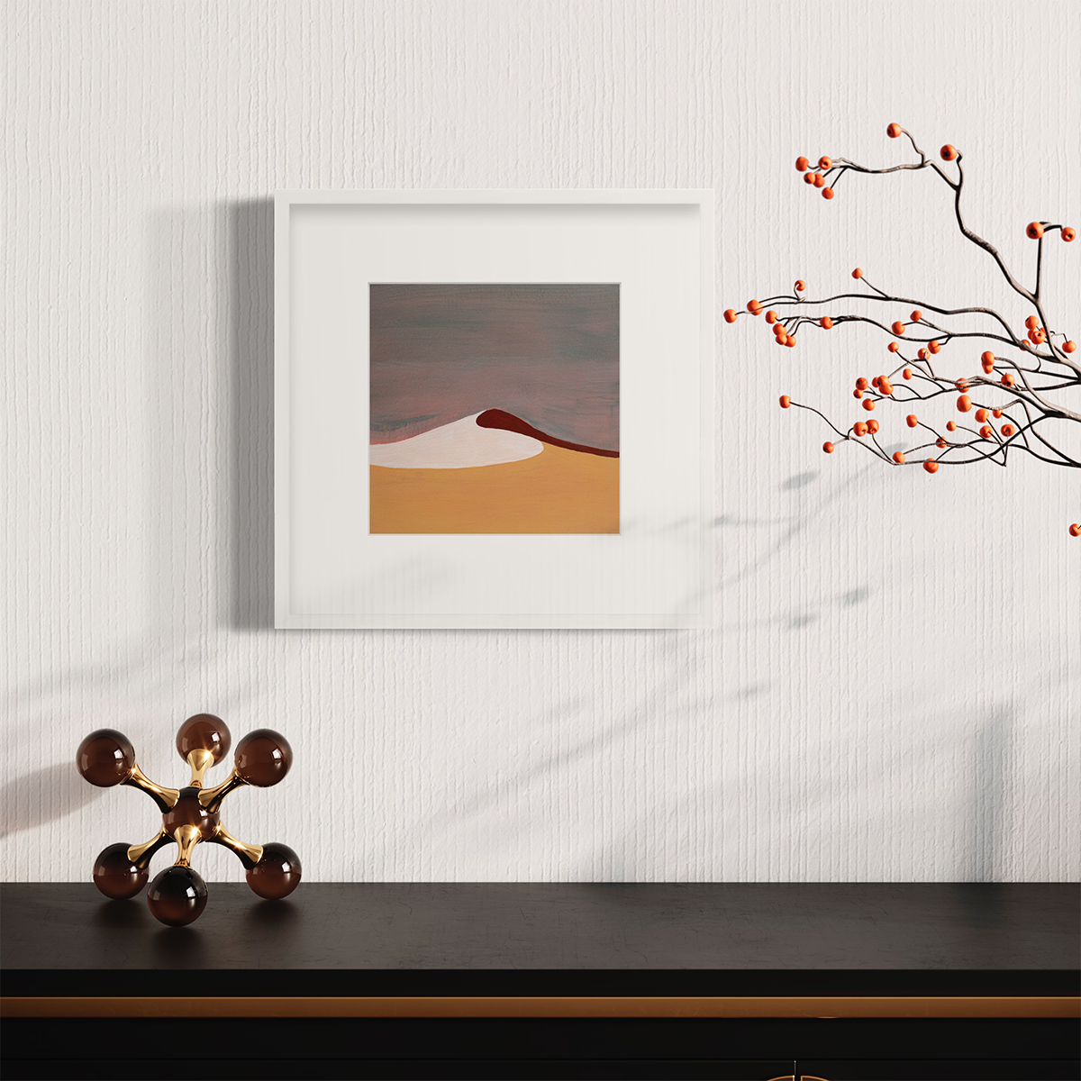 A mauve, burnt yellow, red and white abstract landscape print in a white frame with a mat hangs on a white wall above a black surface with a large decorative jack and orange berries on a stems.