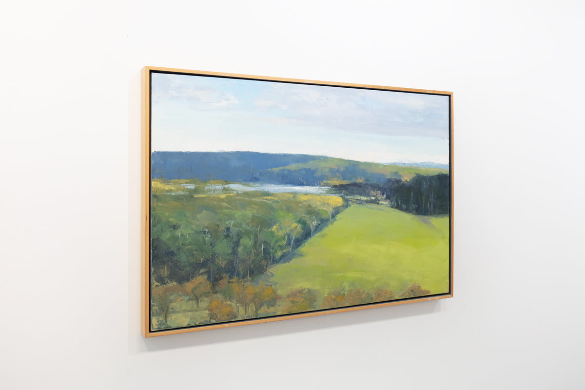 A yellow-green landscape painting in a light wood frame hangs on a light wall.
