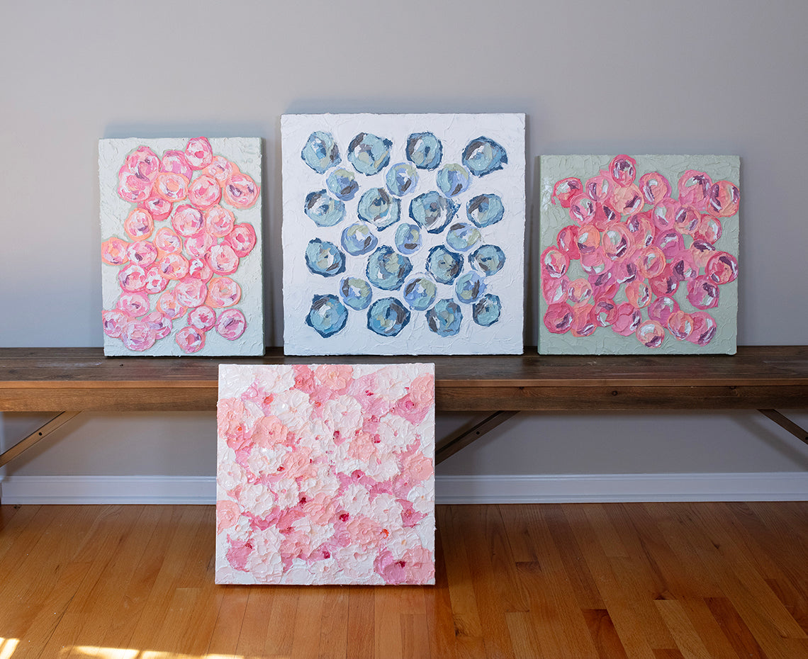 A group of very textured abstract paintings sit and lean on a bench in the artists studio.