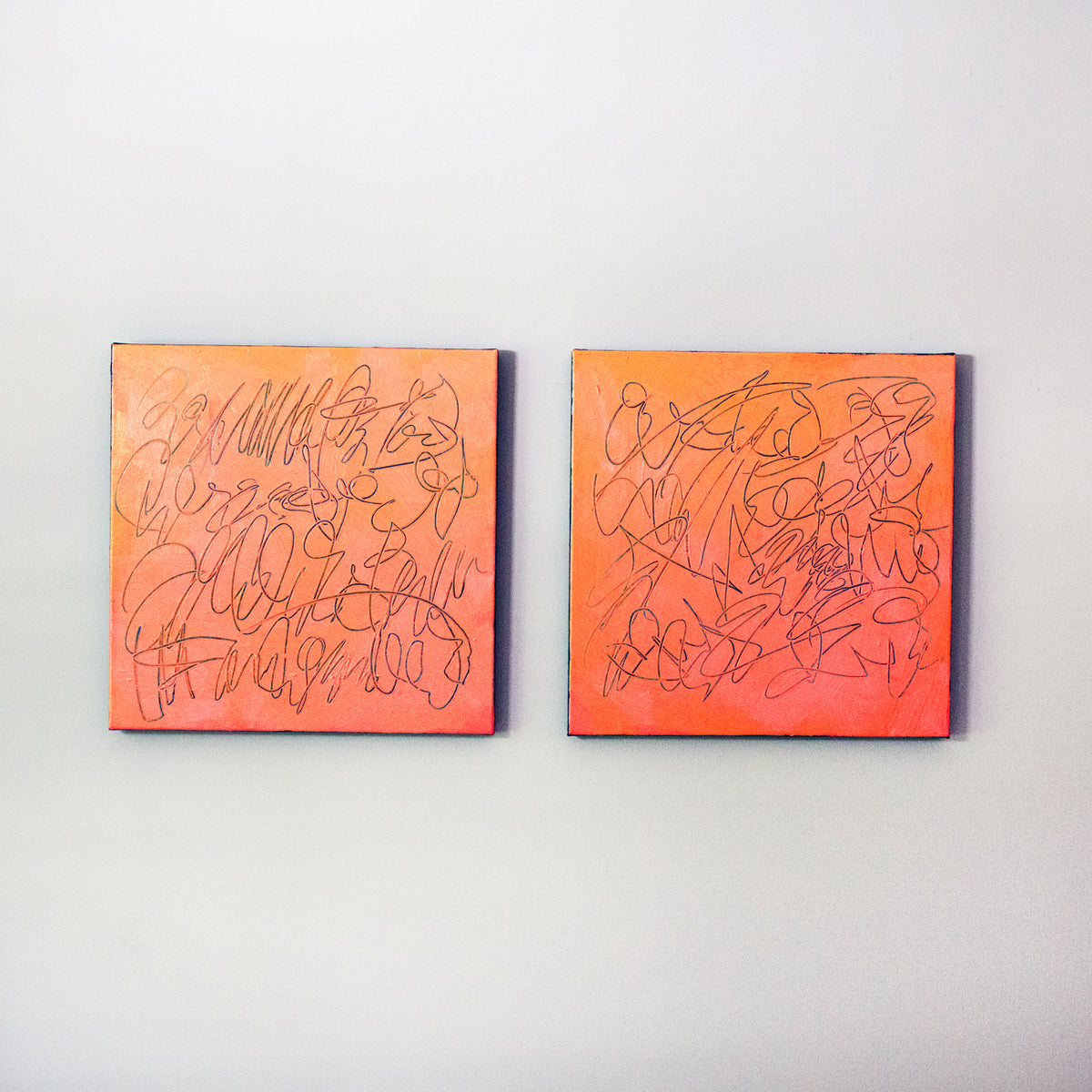 Two square abstract text based paintings with orange and peach gradients, carved into the canvas revealing teal scribbled line art, displayed side-by-side on a light gray wall.
