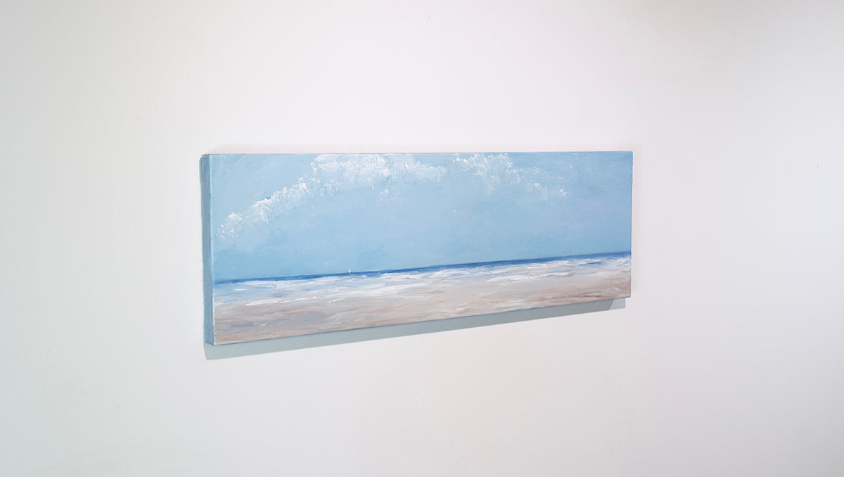 A textured blue and beige coastal painting of a beach hangs on a white wall. 