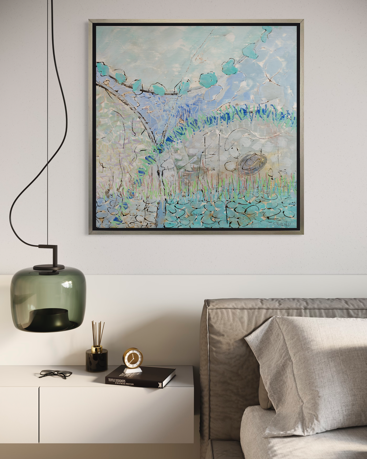 A teal, lavender, black and grey abstract print in a silver floater frame hangs on a white wall above the edge of a grey cushioned headboard with taupe bedding, a green glass pendant lamp and a floating white cabinet shelf with decorative accessories.