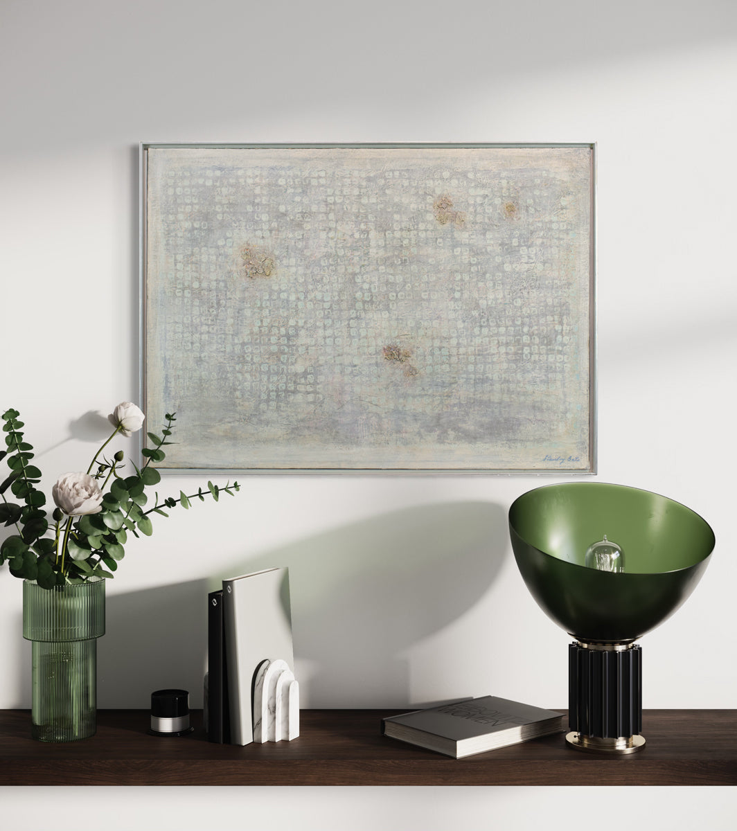 A light grey abstract painting by Stanley Bate hangs on a white wall above a dark wood shelf with modern black and green table decor. 