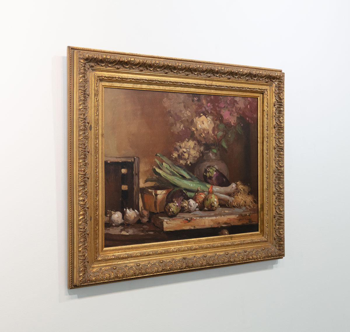 Hyperrealist painting of hydrangeas and vegetables on the table in a gold frame hangs on a white wall viewed from the left.