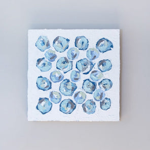 A very textured abstract painting with white background and circle type abstract flowers in blue, teal, green, plum and white hangs on a grey wall.