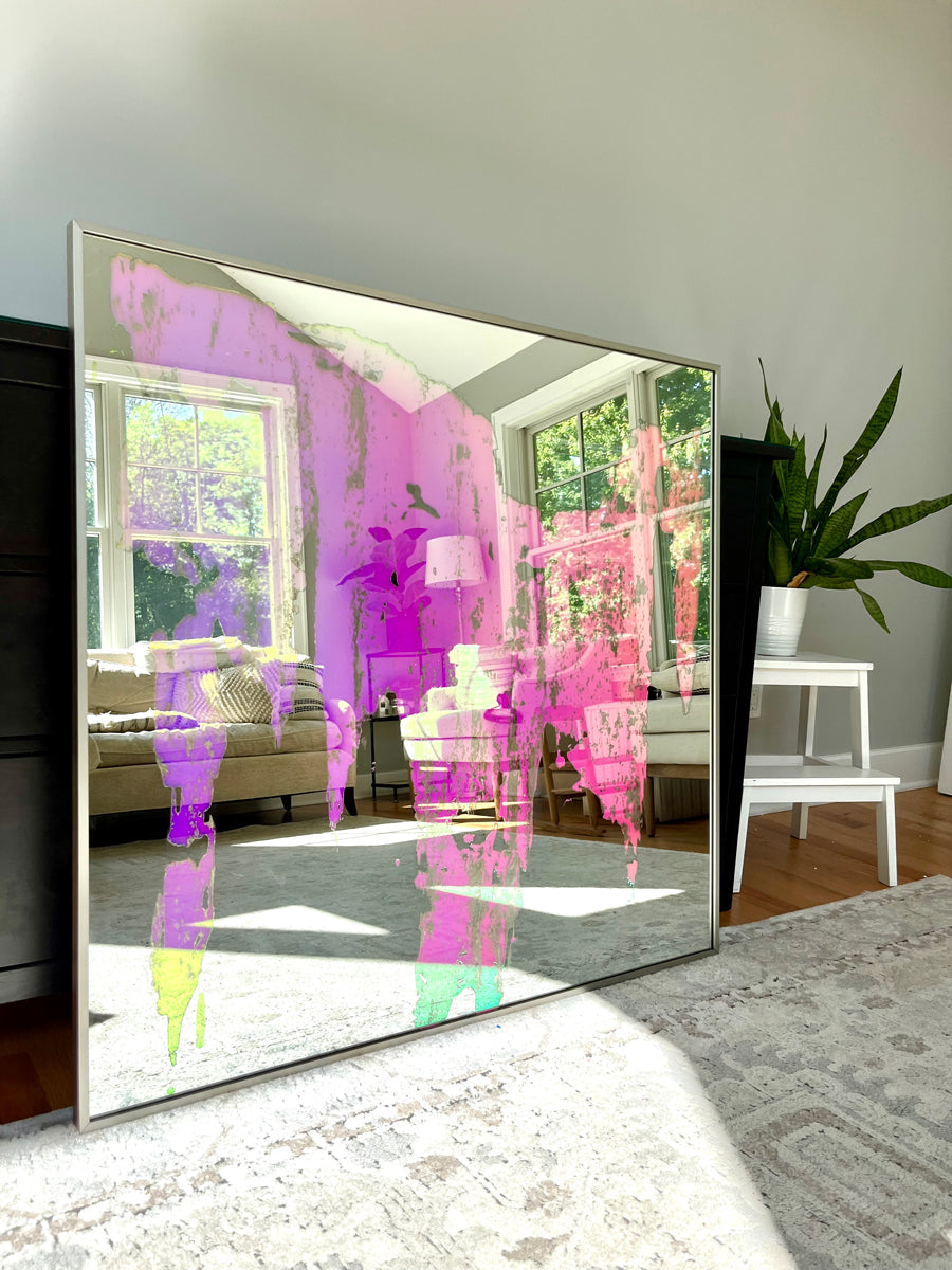 An original fine art mirror by Alina B rests on a carpet against a wood dresser.