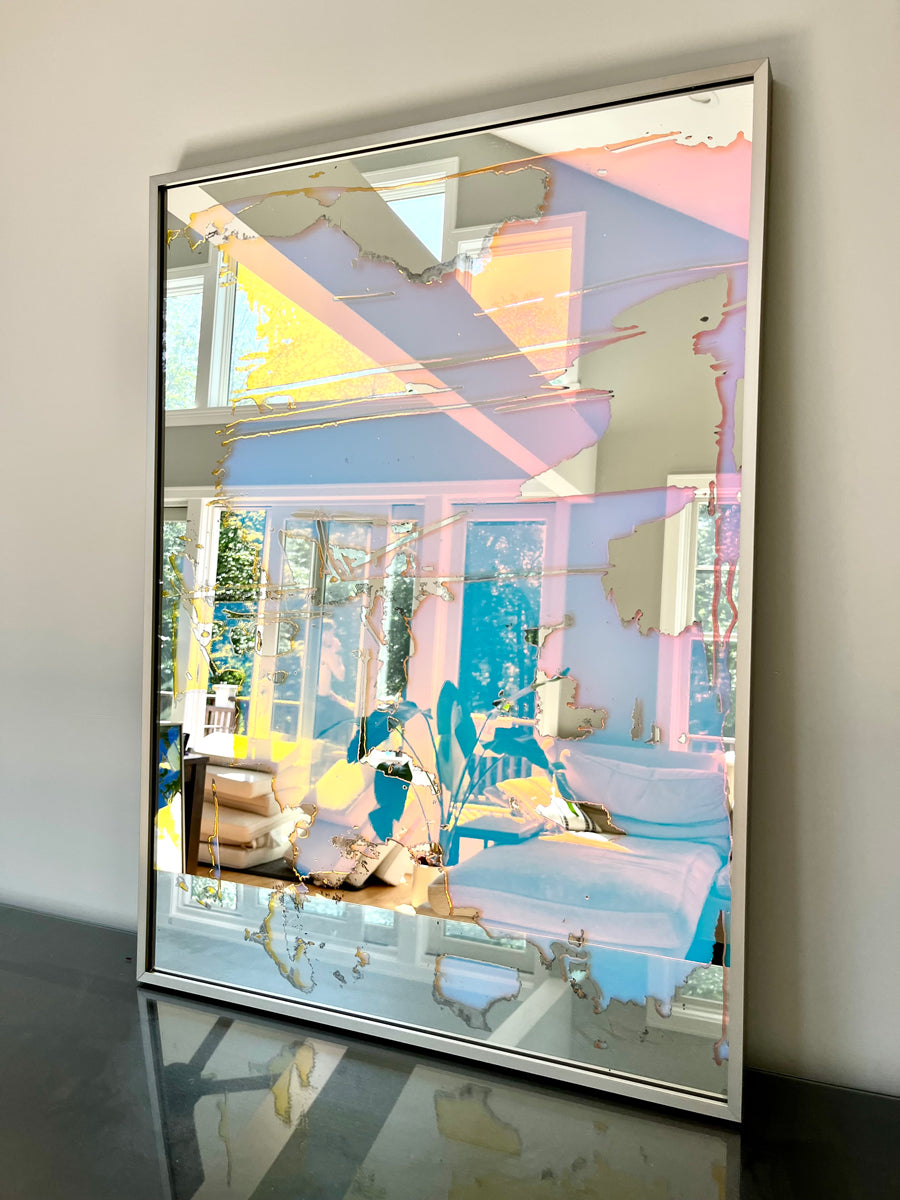A fine art mirror rests on a dark dresser against a wall.