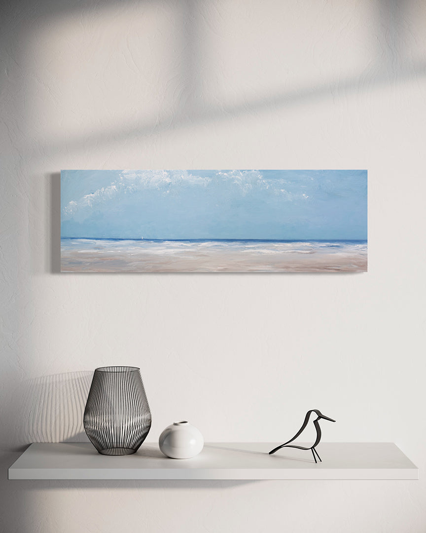 A textured blue and beige coastal painting of a beach hangs on a white wall above a modern white shelf with black and white table decor. 