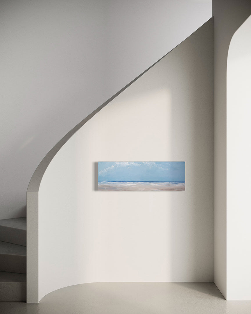 A textured blue and beige coastal painting of a beach hangs on a white wall next to a curved modern staircase. 