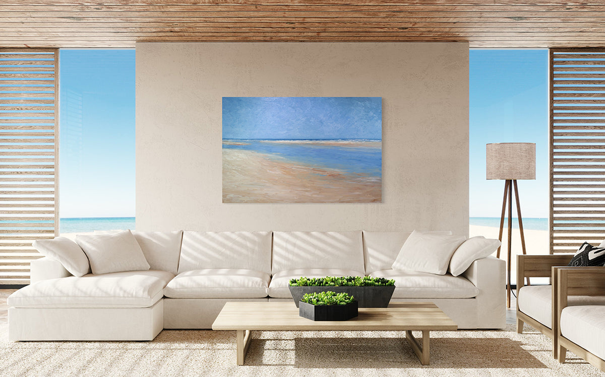 A textured blue and beige coastal painting of a beach hangs on a beige wall above a large white sofa and a light wood coffee table with potted plants. 