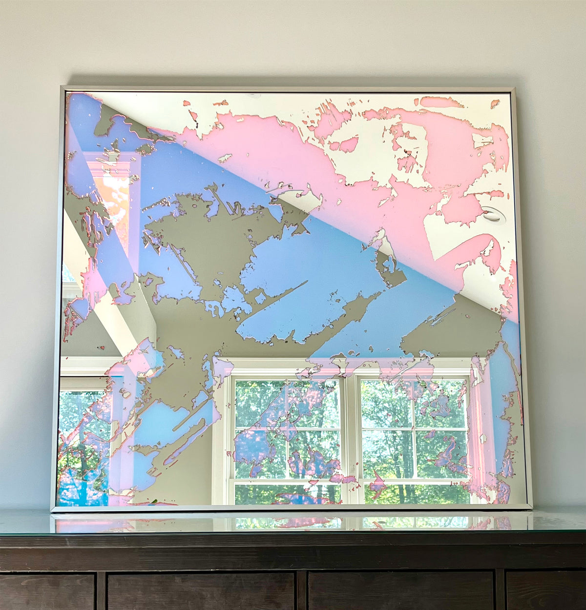 A fine art mirror rests on a wood dresser.