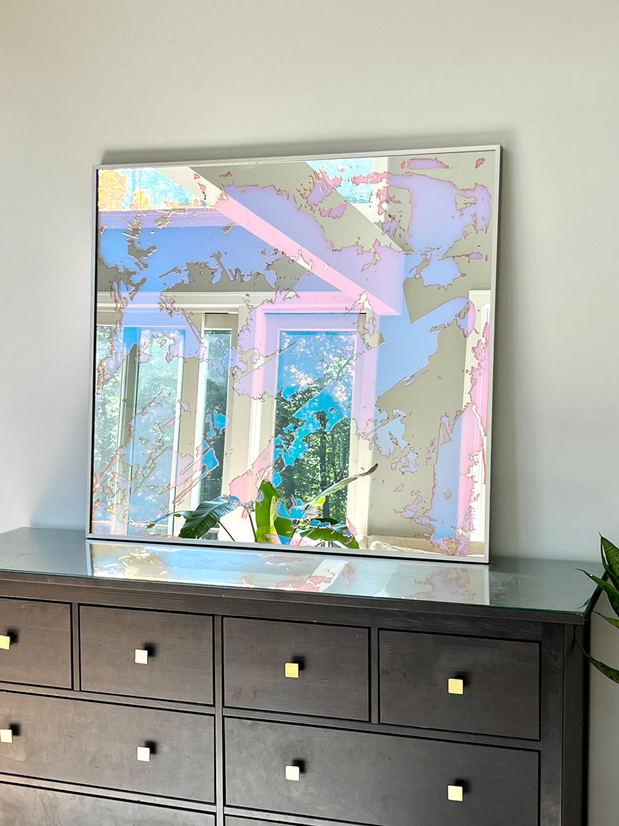 A fine art mirror rests on a wood dresser.