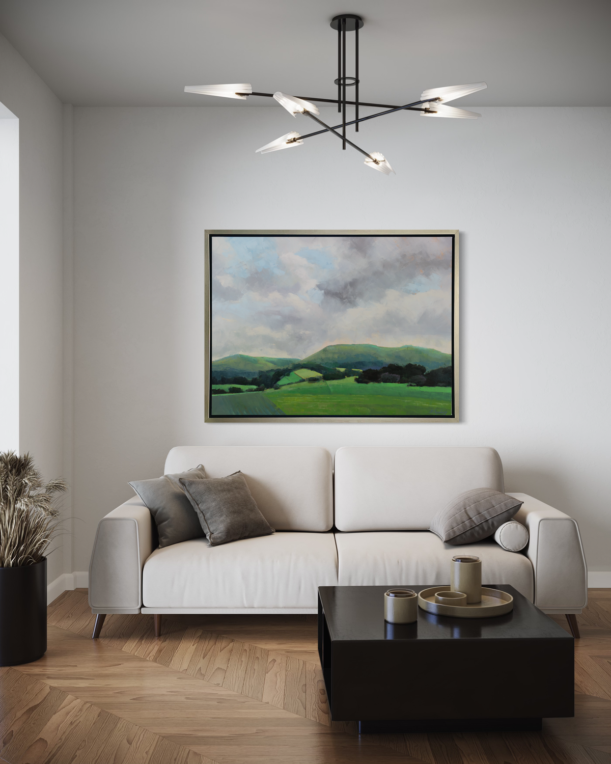 A landscape print in a silver floater frame hangs on a white wall above a white sofa with grey pillows and a square black coffee table.