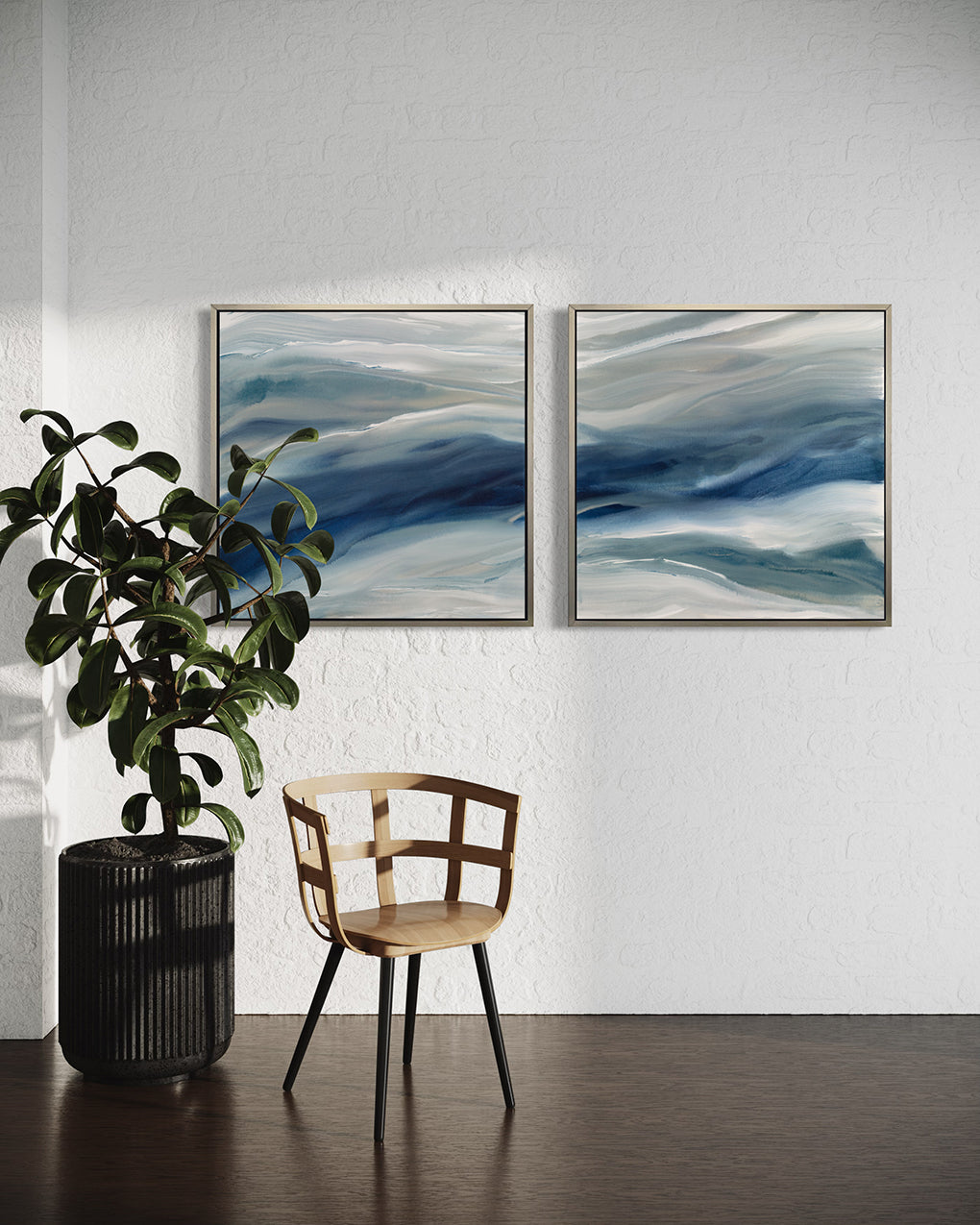 Two blue, teal, beige and white abstract prints in silver floater frames hang on a white wall above a light oak chair and a large potted plant.