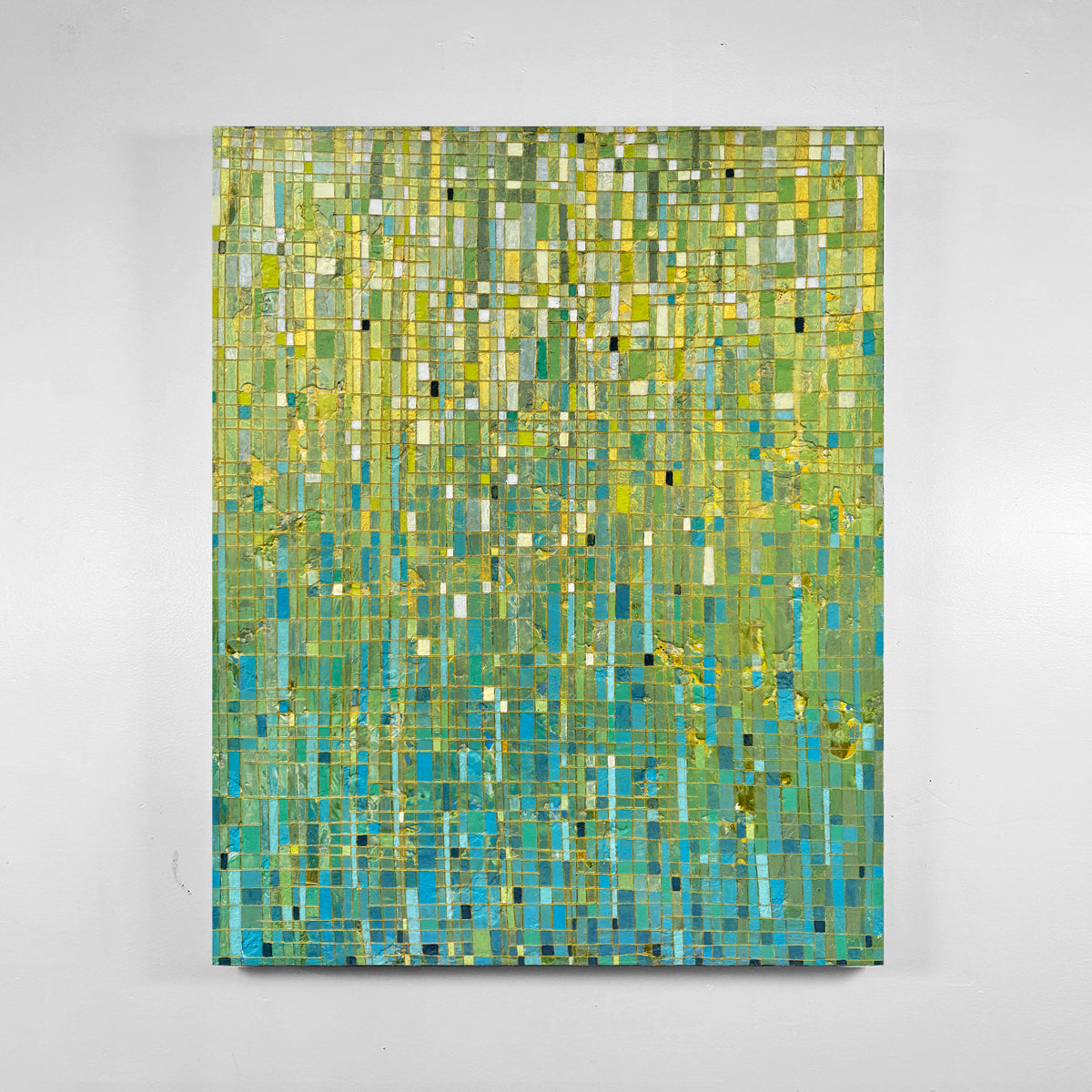 An abstract painting featuring a mosaic grid pattern in shades of green, yellow, and blue, hung on a light gray wall.
